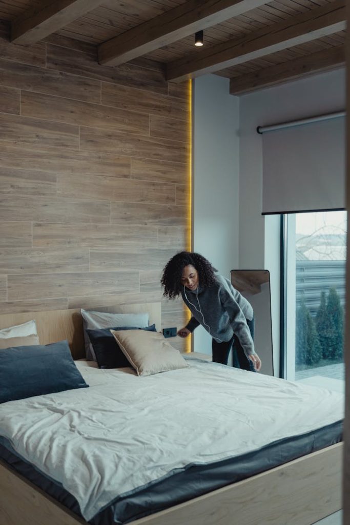 Eco-Cleaning Specialist fixing pillows in a modern bedroom with wooden accents, promoting cleanliness and organization.